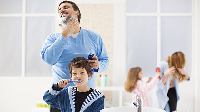 Son washing his teeth while his father shaves