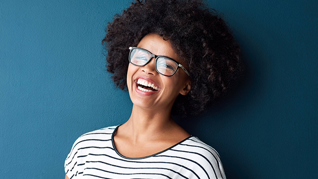 portrait of a smiling girl with curly hair wearing glasses; image used for How Does LED Teeth Whitening Work
